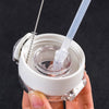 A hand holds a white reusable straw and bottle cleaning brush kit with a clear glass bottle and a plastic straw.