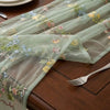 Sheer sage green tulle table runner featuring delicate floral embroidery on a wooden table.