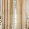 Double layer embroidered beige blackout curtain panels hanging in a light-colored room.