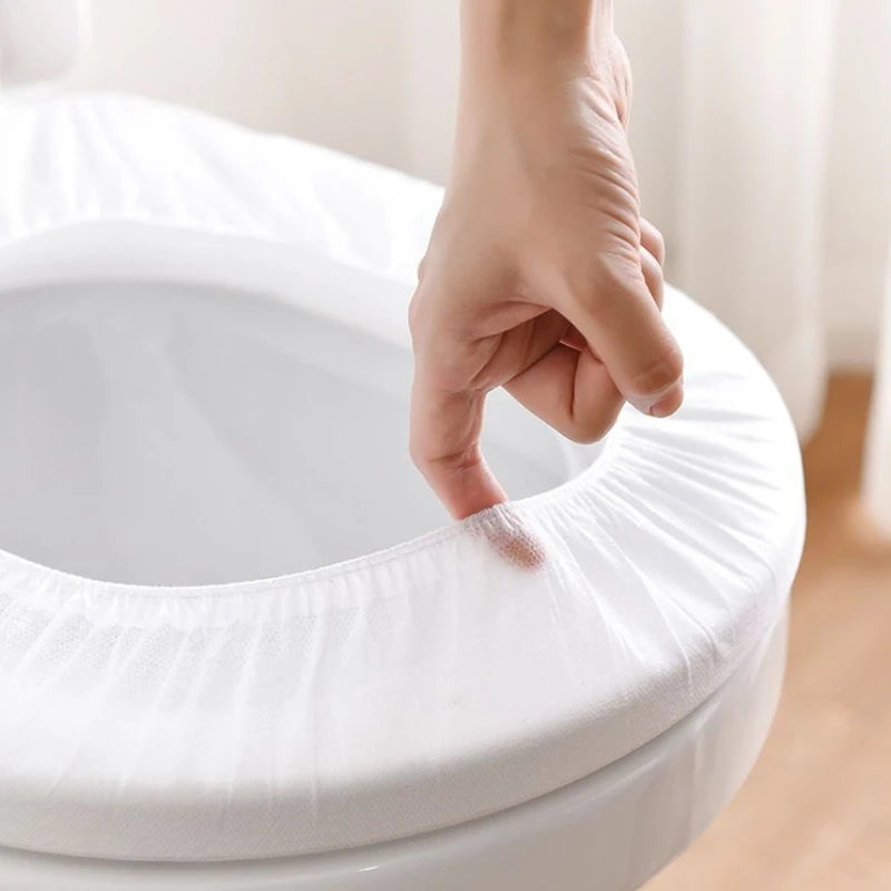 A hand is adjusting a white disposable toilet seat cover on a toilet bowl.