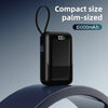 Schwarze, palmkissenförmige Powerbank mit Batteriespeiseanzeige und flexiblem Ring auf blauem Untergrund.