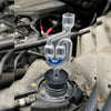 A clear plastic tube with a connector is shown attached to an engine component, likely for combustion leak testing.