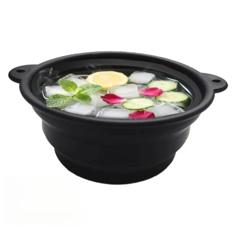 Black foldable silicone ice bath and facial massage bowl filled with ice cubes, lime slices, and rose petals.