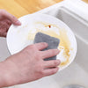 Hands are placing a gray scouring pad onto a white plate in a kitchen sink.