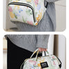 A woman is wearing a light green and white waterproof diaper bag backpack with floral patterns and stroller straps.