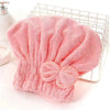 A pink microfiber hair drying towel with a bow-knot head wrap is displayed in a wire basket.