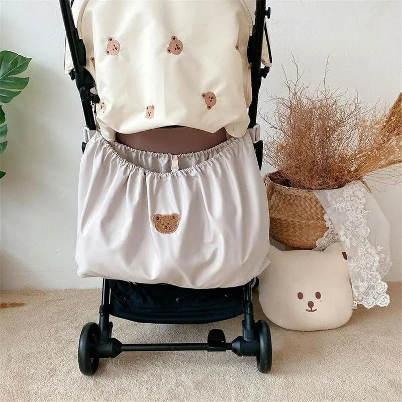 A beige bear-themed stroller organizer bag is shown attached to a black stroller frame.