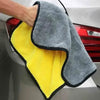 A hand is holding a yellow and gray microfiber cleaning towel with black trim against a car exterior.