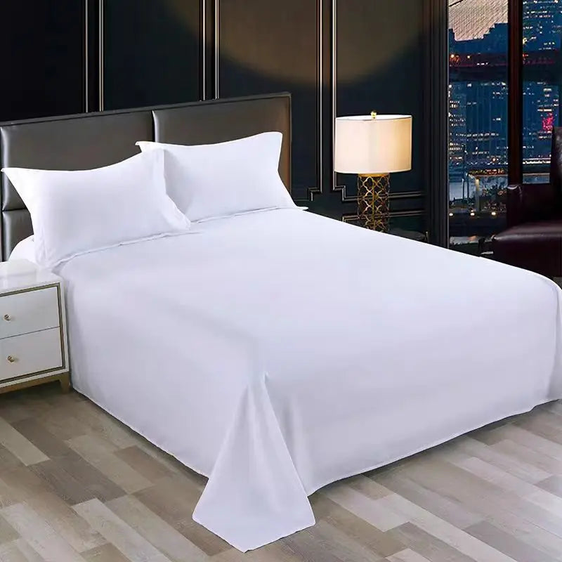 Weiße Premium-Flachbettdecke auf einem Bett mit dunklem Kopfteil und Nachttischlampe.