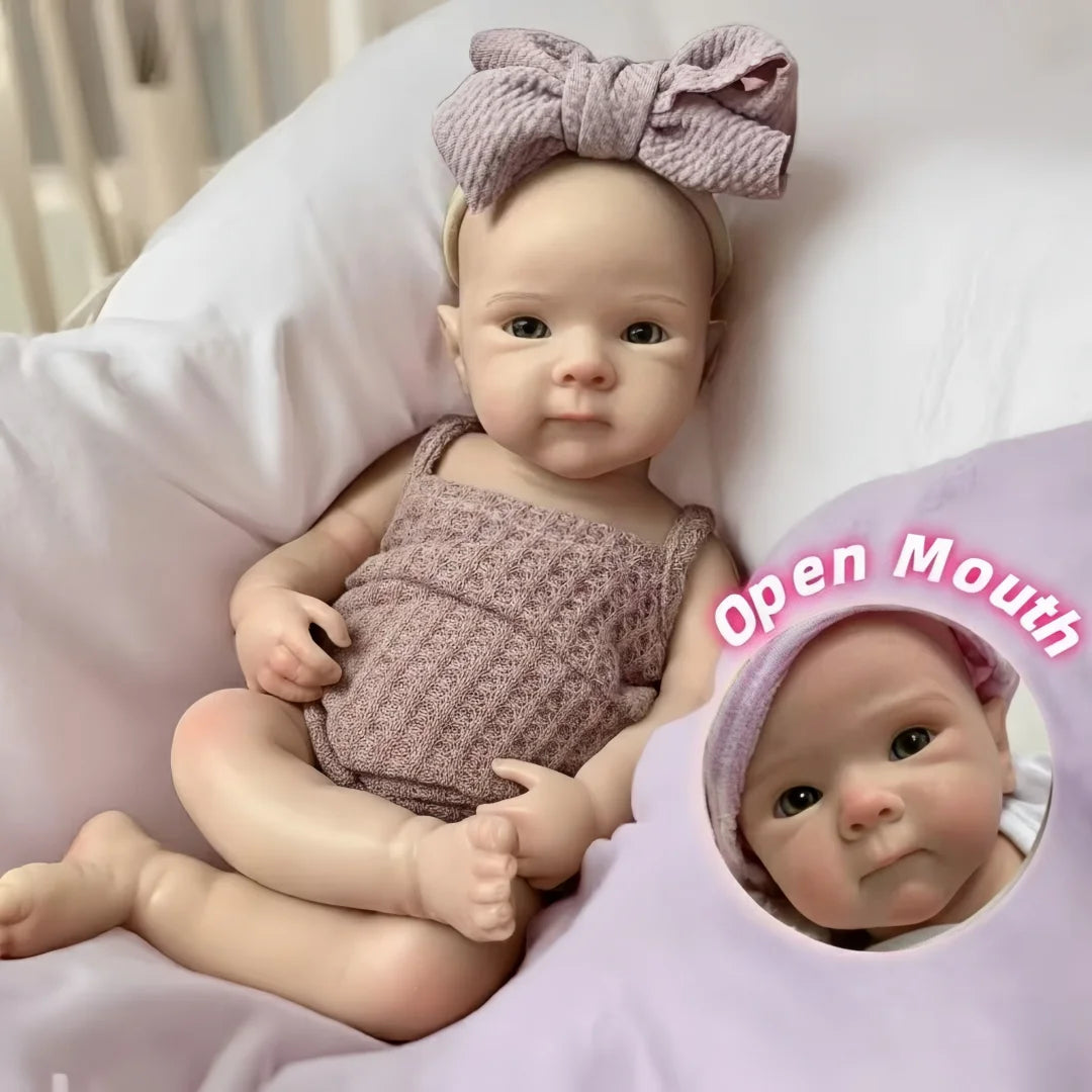 A close-up photo of a newborn silicone reborn doll with a pink bow headband and a knitted outfit lying on a white pillow.