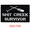 Black embroidered iron-on letter patch featuring a crossed fork and knife design and the text SHIT CREEK SURVIVOR