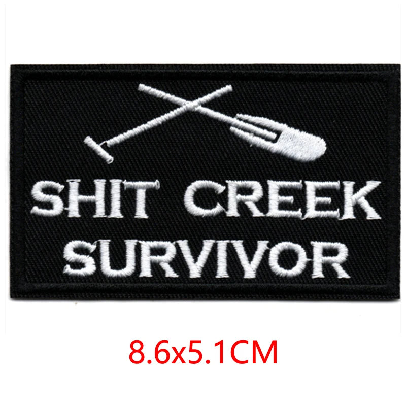 Black embroidered iron-on letter patch featuring a crossed fork and knife design and the text SHIT CREEK SURVIVOR