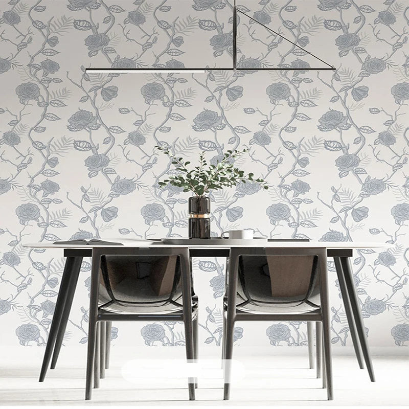 A modern dining table set with a glass top and dark chairs placed against a wall covered in a botanical leaf wallpaper.