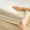 A hand is adjusting a white cotton fitted sheet with an elastic band on a bed.