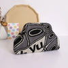 A hand-knit clutch bag featuring a gray and black abstract pattern with white accents, placed next to a light beige fabric pi