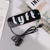 A black USB-powered LED taxi sign with multiple light bulbs and a cable lying next to a book.