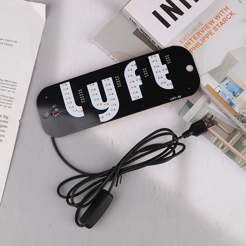 A black USB-powered LED taxi sign with multiple light bulbs and a cable lying next to a book.