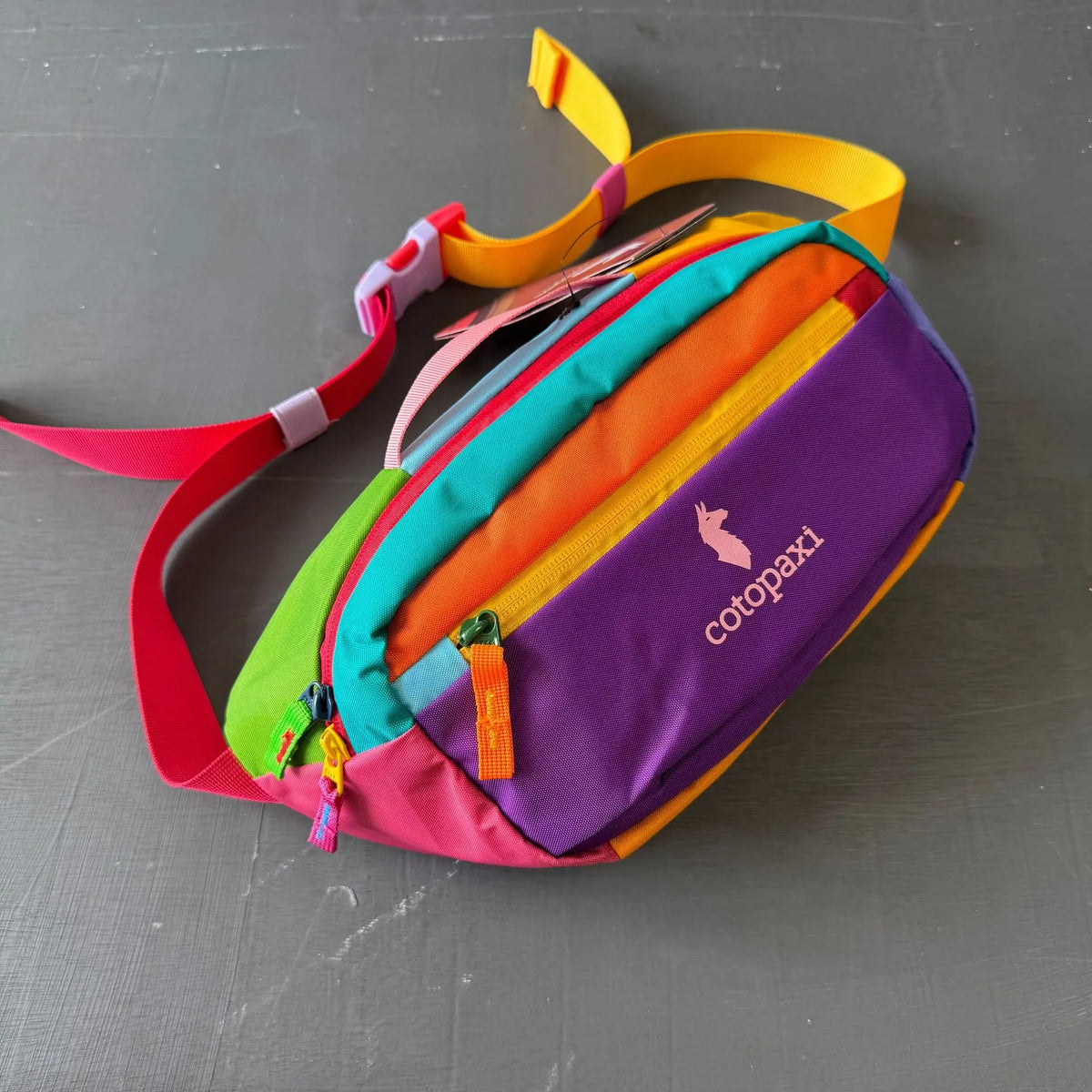 A color block waterproof nylon fanny pack featuring vibrant stripes of pink, red, orange, yellow, and purple.