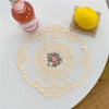 Elegant oval lace embroidered placemat with a yellow lemon and a glass bottle on a white table.