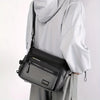 A person is holding a black men's water-resistant nylon crossbody sling bag against a white background.