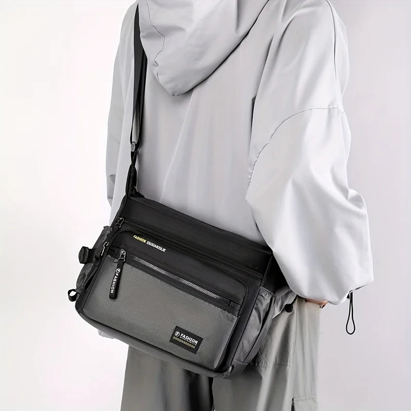 A person is holding a black men's water-resistant nylon crossbody sling bag against a white background.