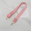A pink nylon bag strap with a gold buckle is displayed on a white marble surface.
