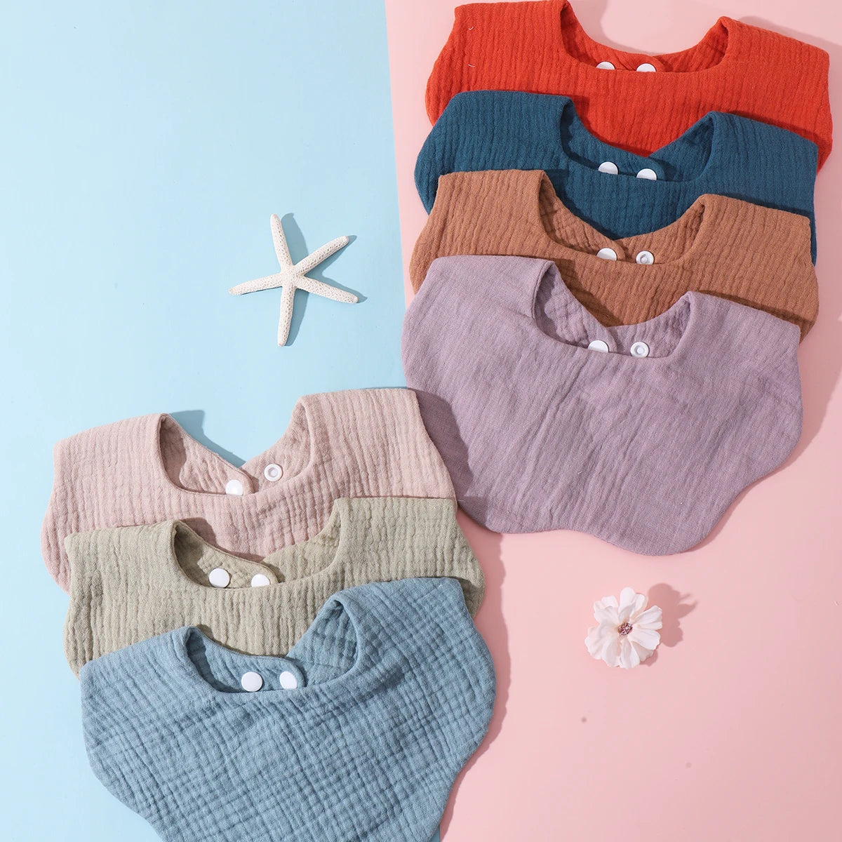 A flat lay of a 3-pack of soft cotton baby bibs in various colors including orange, blue, brown, purple, and green.