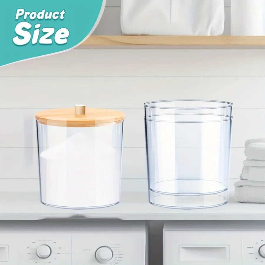 Clear acrylic detergent pod storage container with a wooden spoon on a white shelf.