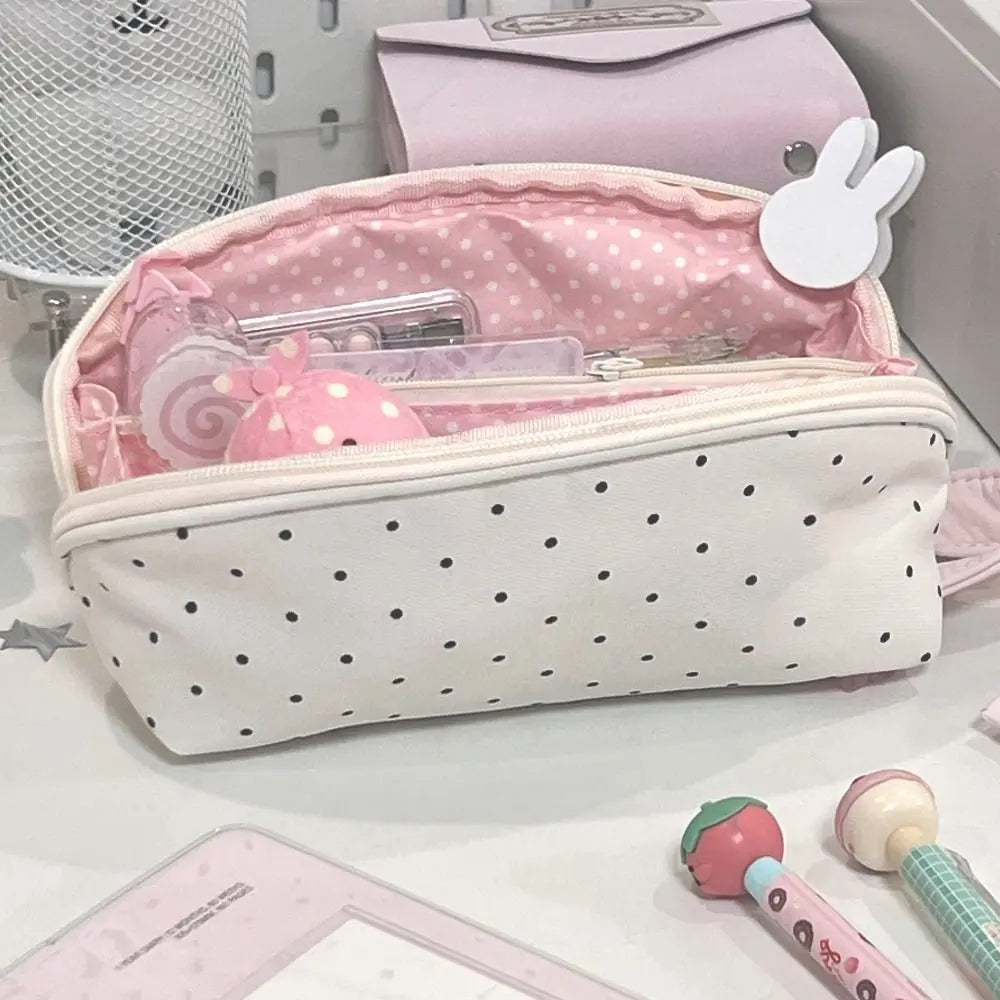 A pink and white polka dot shell-shaped pencil case with multiple compartments is shown on a white surface.