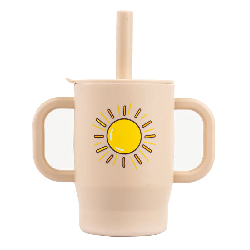 A light beige silicone training cup with a straw and handles featuring a yellow sun design.