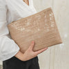 A beige crocodile-embossed PU leather envelope clutch held by a person wearing a white shirt.