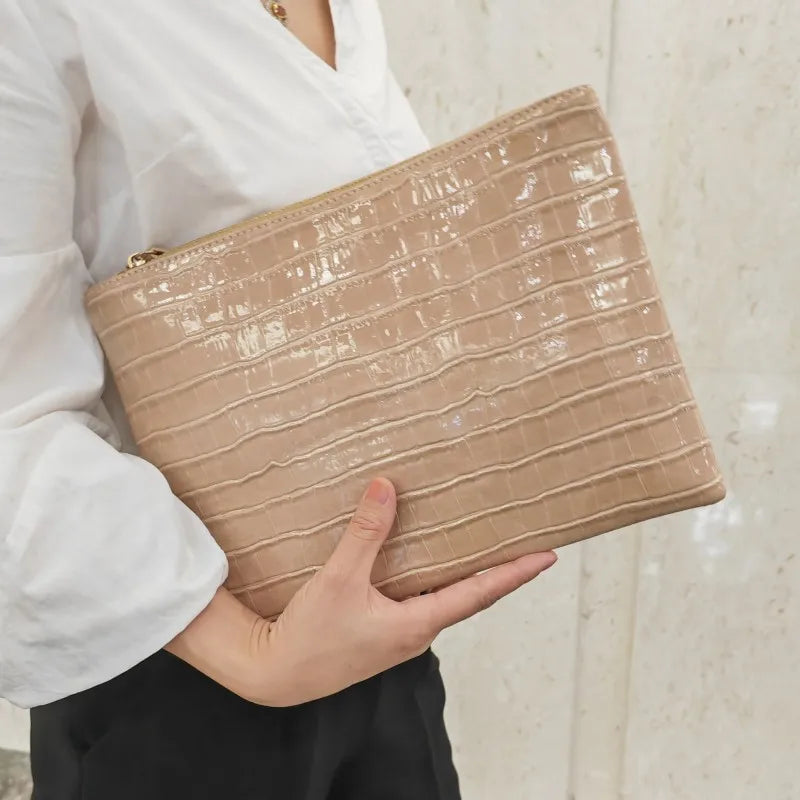 A beige crocodile-embossed PU leather envelope clutch held by a person wearing a white shirt.