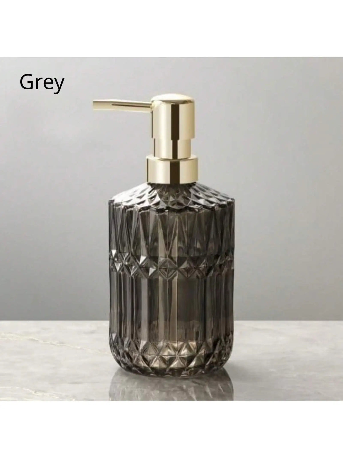 A clear glass soap dispenser with a gold pump top, set against a grey background.