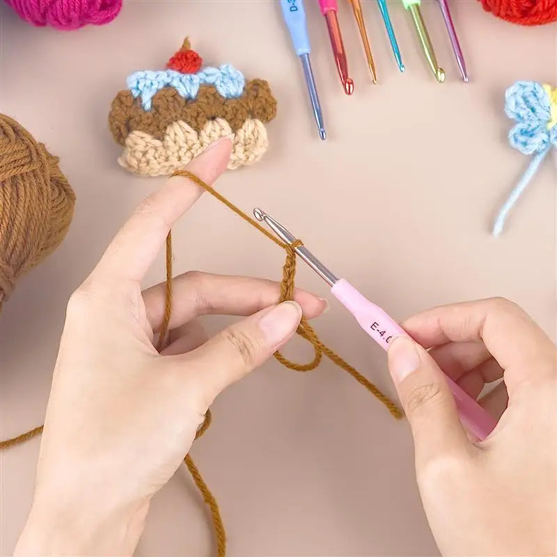 A hand is using a pink crochet hook to thread yarn, next to a set of colorful aluminum alloy crochet hooks and a crocheted ca