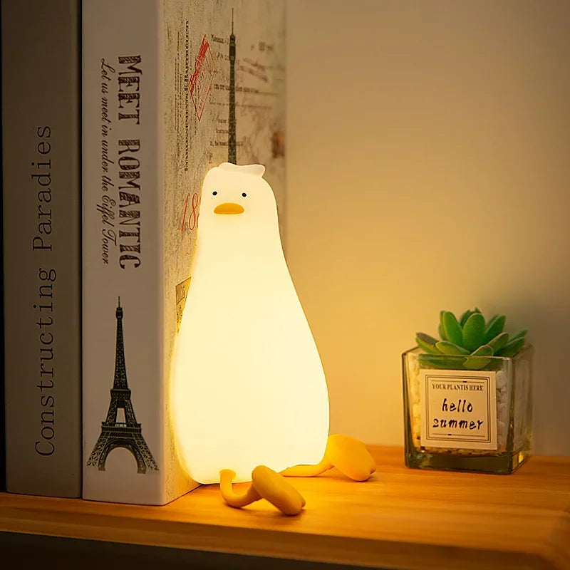 A white silicone duck touch night light illuminates a small green succulent plant on a wooden surface.