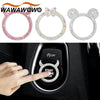 A hand presses the start button on a car ignition, next to various rhinestone-encrusted rings.