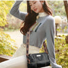 A woman models a black vintage genuine leather shoulder bag with gold accents and white pants in an outdoor setting.