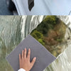 A hand holds a gray microfiber cloth against a glass surface, showing the texture of the cloth and a reflection.