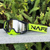 A pair of neon yellow and black HD Motocross goggles resting on a light surface amidst green foliage.