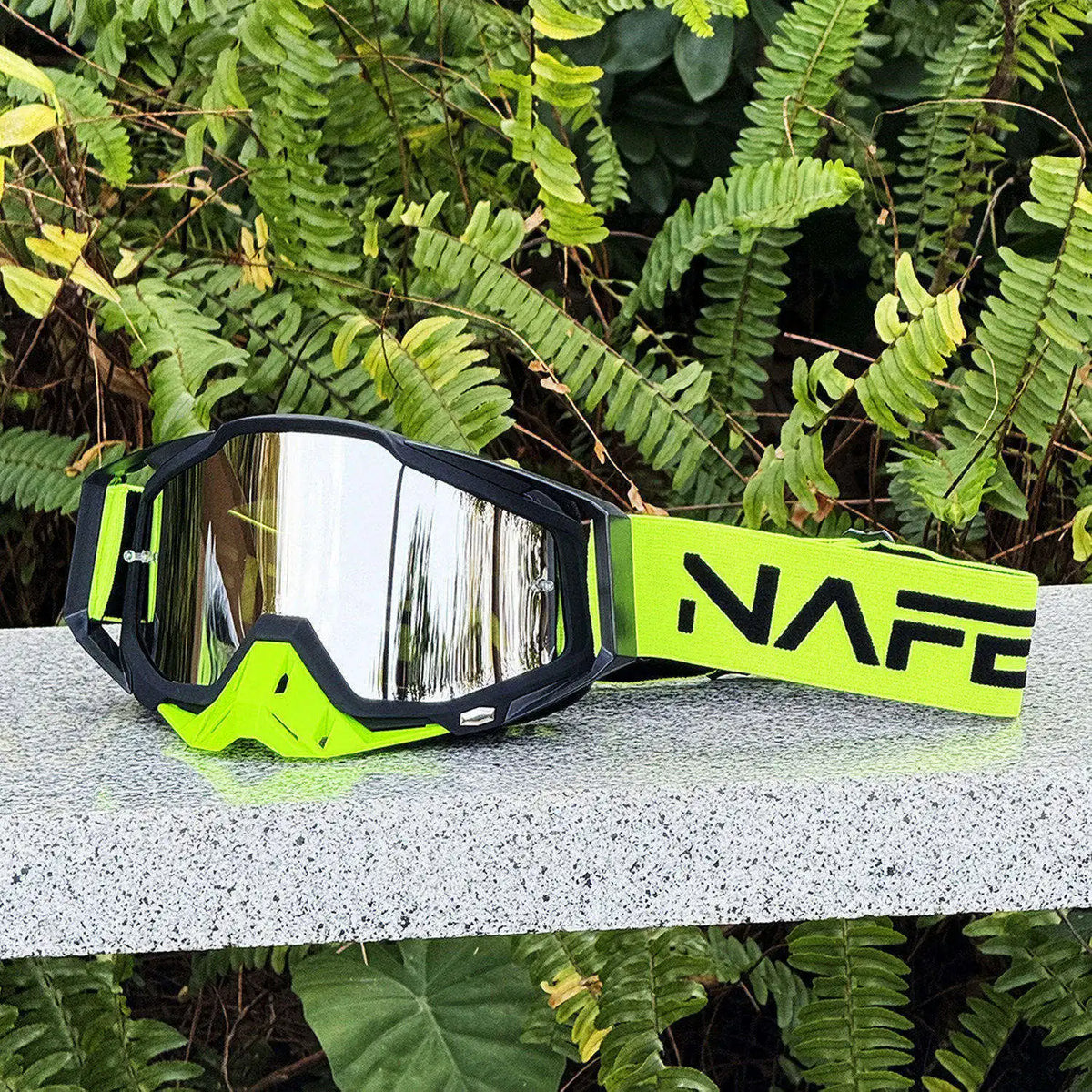 A pair of neon yellow and black HD Motocross goggles resting on a light surface amidst green foliage.