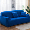 A vibrant blue elastic stretch sofa cover for a 3-seater sofa with two accent pillows, displayed in a bright room.