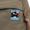 A black and red cartoon penguin enamel pin is attached to a canvas fabric, showing the name NOOT in blue text.