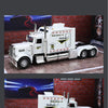 A white 1:24 scale diecast Peterbilt 389 heavy truck model with pull-back action, sound, and lights displayed on a brick back