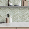 A kitchen shelf displaying various wooden and ceramic kitchen tools against a pale green chevron patterned backsplash.