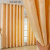 A close-up of a flowing, sheer gold curtain with a feather jacquard pattern hanging indoors.