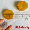 A yellow magnetic strategy game piece shaped like a hexagon, shown next to a ruler and a hand.