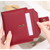 A close-up of a maroon leather bifold wallet with a clear plastic sleeve and gold-toned snaps being held by a hand.