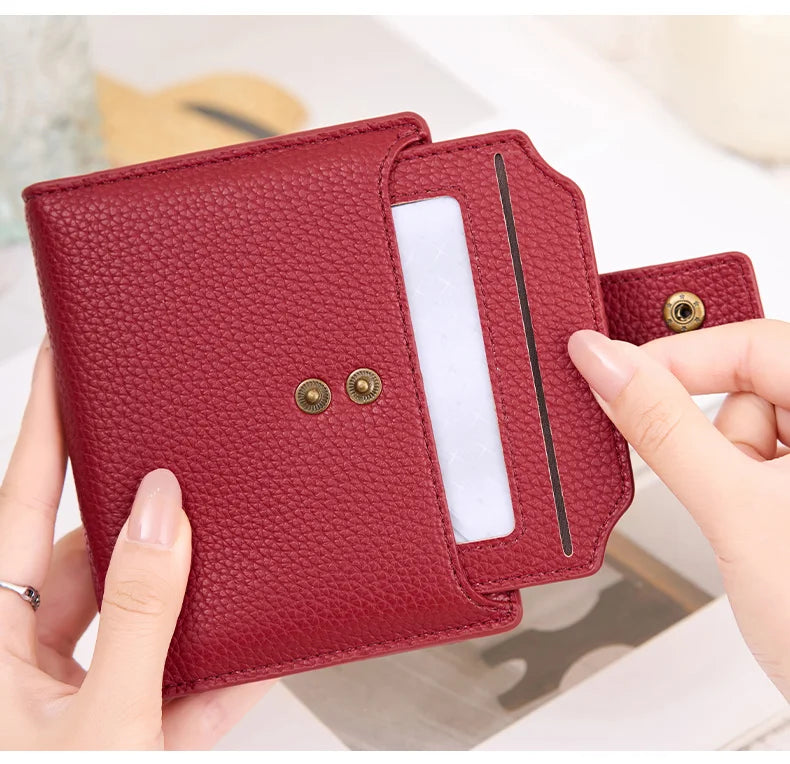 A close-up of a maroon leather bifold wallet with a clear plastic sleeve and gold-toned snaps being held by a hand.