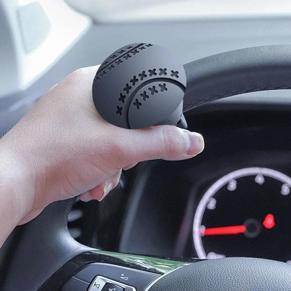 A hand is grasping a black steering wheel knob designed for one-hand control inside a car interior.