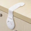 White child safety cabinet lock with a strap and release mechanism mounted on a wooden cabinet door.